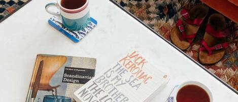 Ein Buch mit dem Titel „Jack Kerouac ist mein Meer“ auf einem weißen Tisch zusammen mit zwei Teetassen und einem Paar Sandalen.
