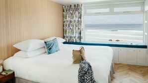 A bedroom with a large bed, a view of the ocean, and a window with curtains. - 6 Barnaloft (St Ives)