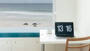 Un ordinateur portable est posé sur un bureau, et par la fenêtre, on peut admirer la plage et l’océan.