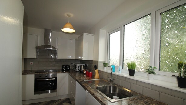 A modern kitchen with a stainless steel range hood, a built-in oven, a double sink, and a window with a view of greenery.
