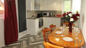A modern kitchen with white cabinets, a wooden dining table set for four, and a red curtain on the left.