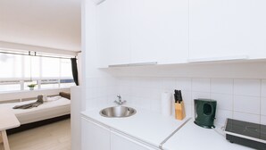 A modern kitchen with white cabinetry, a stainless steel sink, and a black induction cooktop. - Bright Studio Flat in Central London Zone 1 Paddington / Lancaster gate cozy (London)