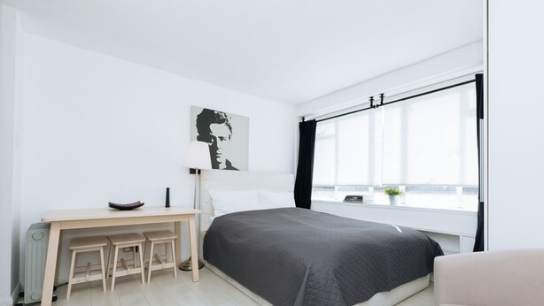 A modern bedroom with a large bed, a desk with two stools, a radiator, and a window with a view. - Bright Studio Flat in Central London Zone 1 Paddington / Lancaster gate cozy (London)