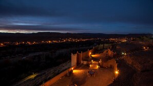 Nachtsicht auf ein historisches Gebäude mit Innenhof, Steinmauern und einem gepflasterten Bereich mit Tischen und Stühlen.