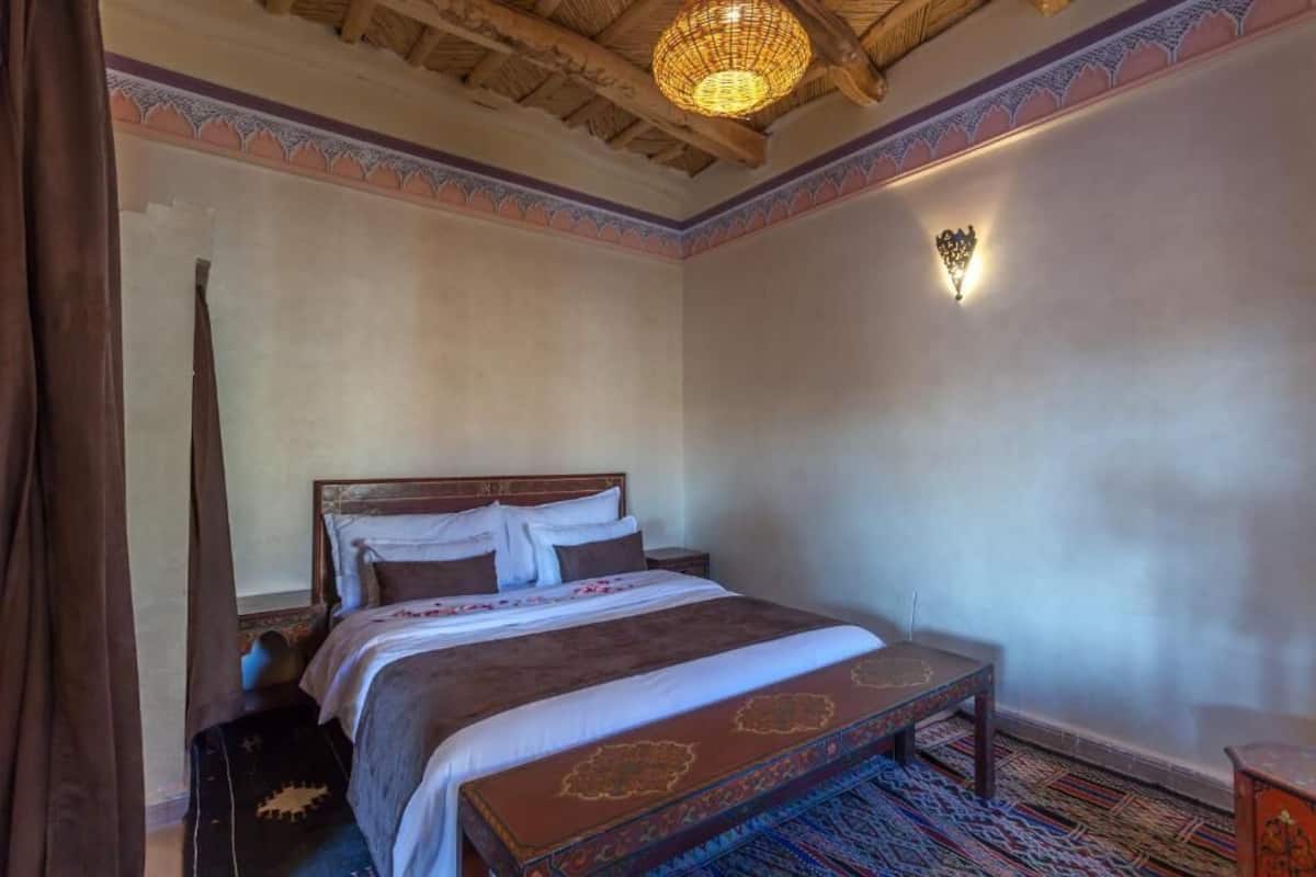 Une chambre traditionnelle avec un lit, une table de chevet, une lampe fixée au mur et un tapis à motifs.