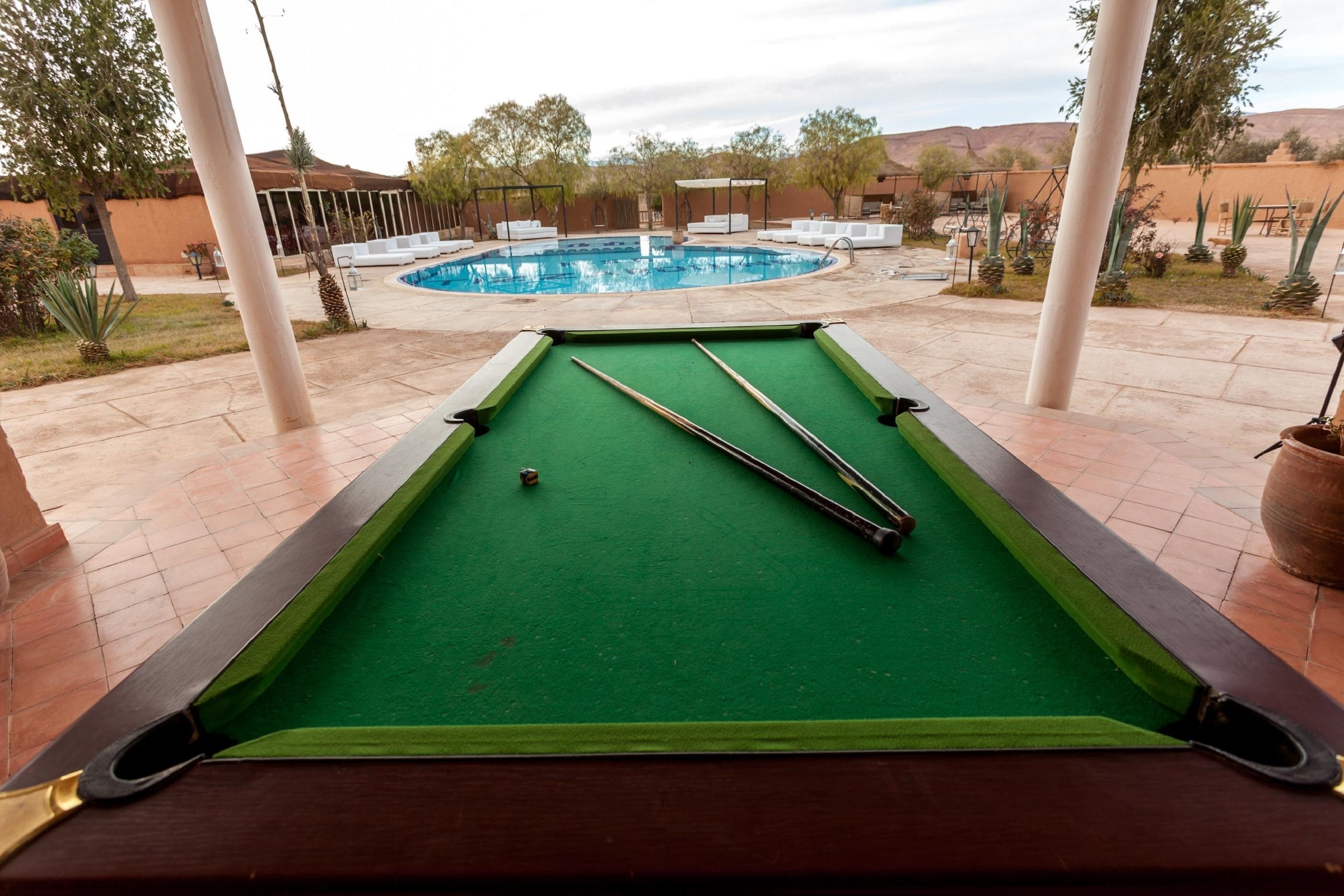 A pool table with pool cues and a pool in the background.