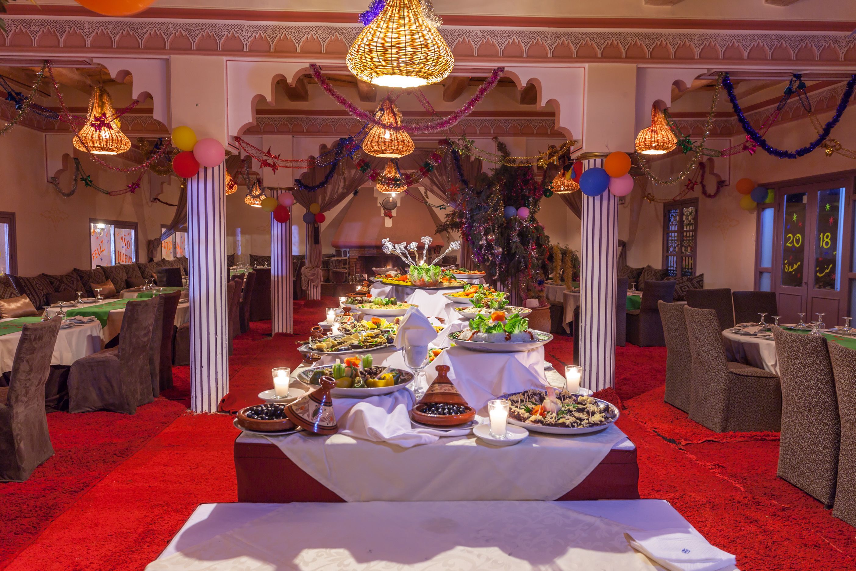 Un salón de banquetes con mesas dispuestas para una comida, decorado con luces colgantes y globos.