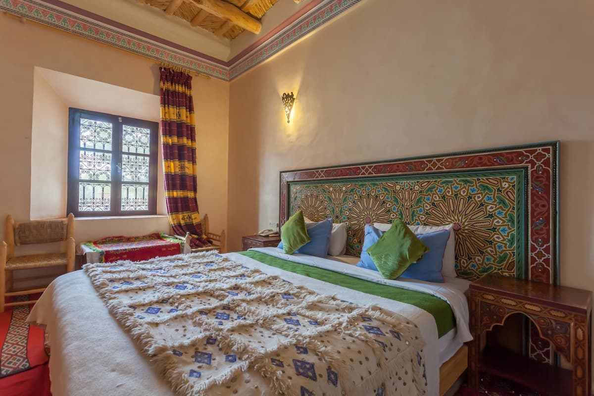 Une chambre à coucher comprenant un lit, une chaise, une table, une fenêtre avec des rideaux et un mur décoratif.