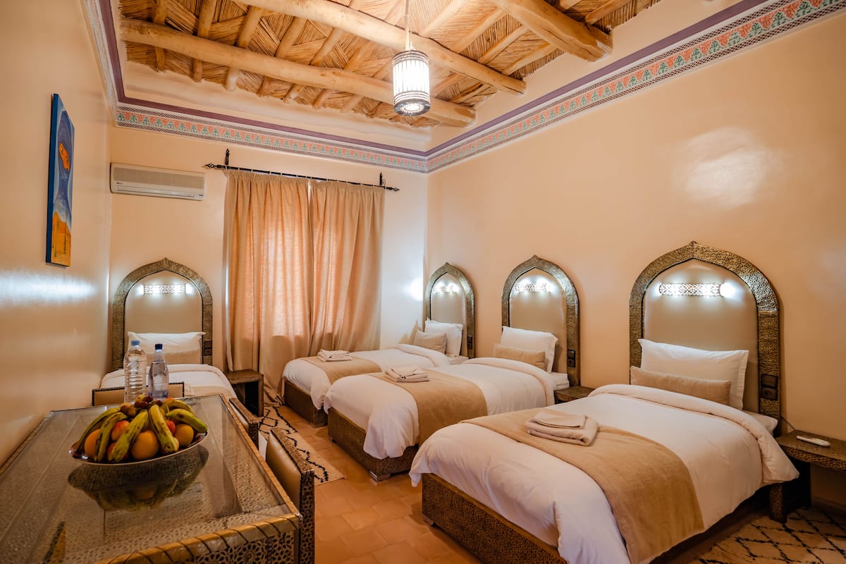 Une chambre d’hôtel avec deux lits, un panier de fruits sur une table et un ventilateur de plafond.