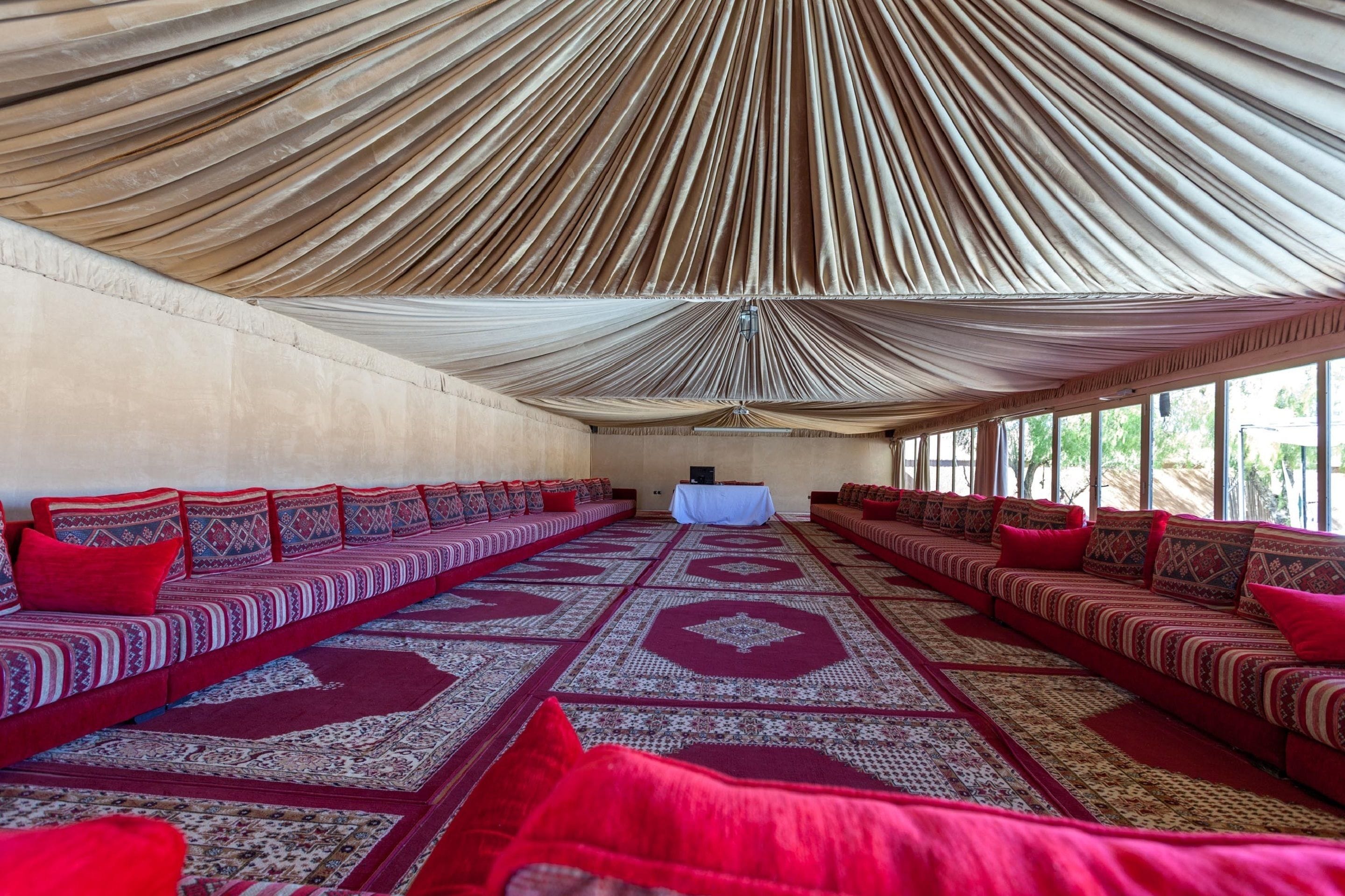 Een ruime, open zaal met een hoge plafond en een kamerbreed tapijt. Er staan meerdere rijen rode en beige gestoffeerde zitplaatsen langs de muren.
