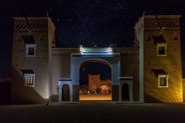 Un edificio histórico con un amplio arco de entrada, un letrero que indica que es un hotel y restaurante, y un cielo nocturno estrellado.