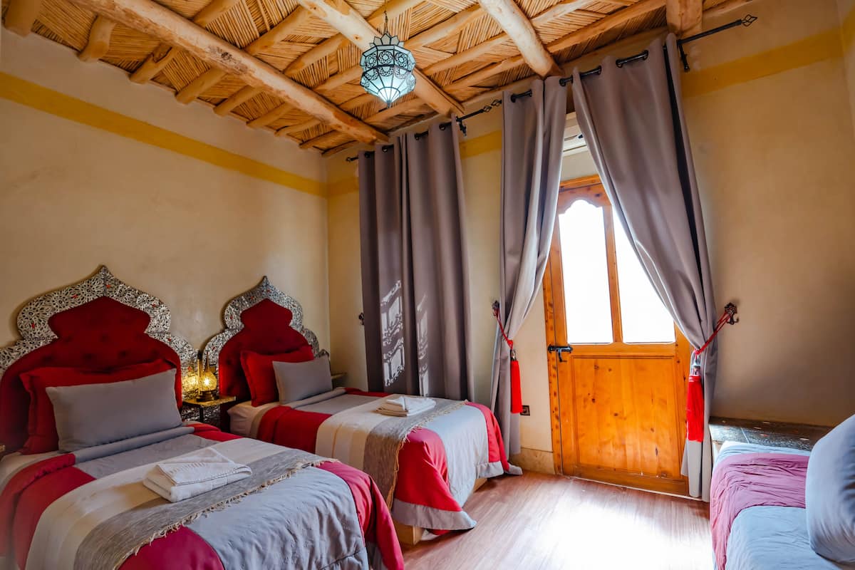Une chambre avec deux lits, un plafond en bois et une grande fenêtre avec des rideaux.