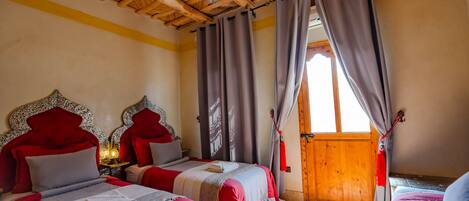 A room with two beds, wooden ceiling, and a large window with curtains.