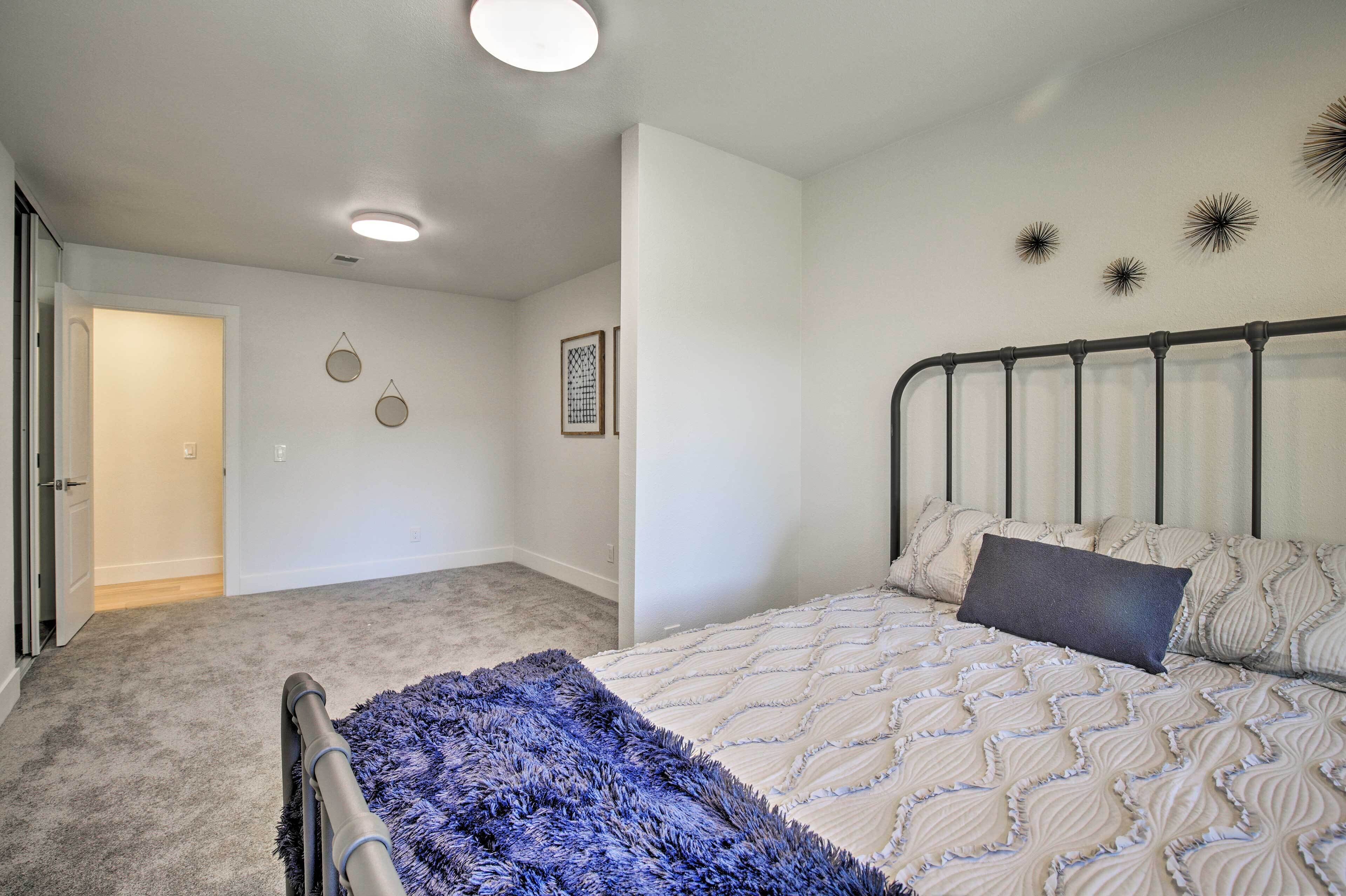 Une chambre à coucher avec un lit, un plaid bleu, un mur blanc orné d’objets décoratifs et une porte donnant sur une autre pièce.