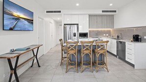 Una cocina moderna con armarios blancos, una isla central con taburetes altos, horno empotrado y un televisor de pantalla plana grande montado en la pared.