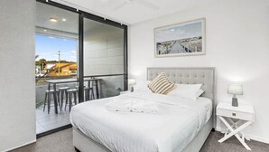 Un dormitorio moderno con una cama grande, un ventanal corredero a un balcón y un cuadro enmarcado en la pared.