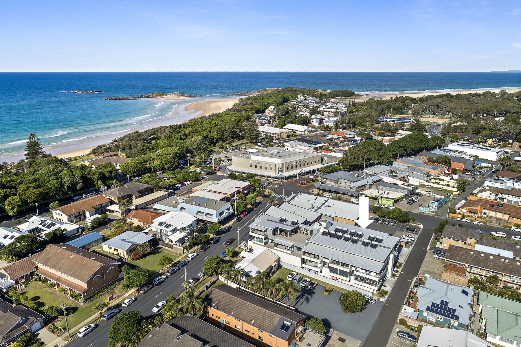 An aerial view of a coastal town with a beach, residential buildings, and a hotel with a large sign.