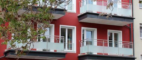 A red multi-story building with balconies, windows, and a door.