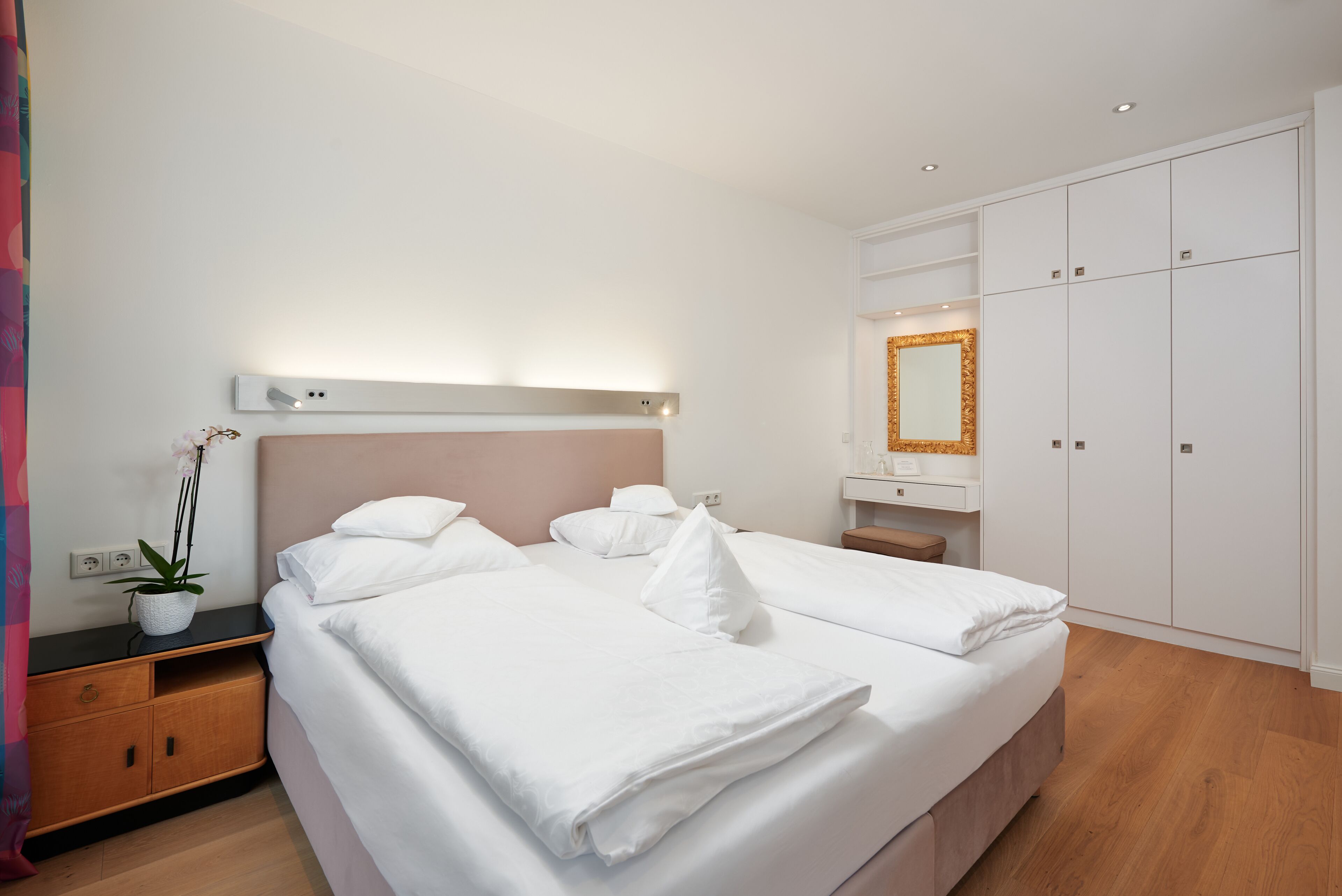 Une chambre d’hôtel moderne avec un lit double bien fait, une table de chevet avec une lampe, une petite plante en pot et une grande armoire.