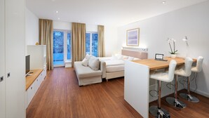 A modern living room with a sofa, a dining area with a table and chairs, and a large window with curtains.