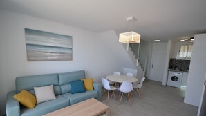 Moderni olohuone, jossa on vaaleansininen sohva, puinen sohvapöytä ja ruokailutila, jossa on pyöreä pöytä ja valkoiset tuolit.