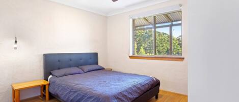 A bedroom with a bed, a wooden bench, a ceiling fan, and a window with a view of trees.