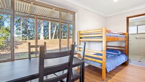 Ein Zimmer mit einem Etagenbett, einem Schreibtisch und einem Stuhl. Ein Fenster bietet Blick auf Bäume und einen Feldweg.