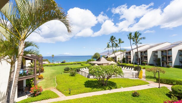 A resort with a well-maintained lawn, palm trees, and a view of the ocean.