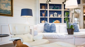 Uma sala de estar moderna com um sofá branco, uma poltrona de couro, uma mesa redonda e um vaso com planta.