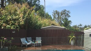 Ein Garten mit Schwimmbad, einer Holzterrasse und einem eingezäunten Bereich mit Stühlen und einem Tisch.