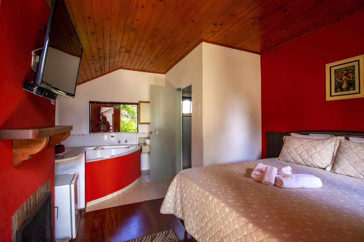 Ein Schlafzimmer mit Bett, roter Wand, Holzboden und einem Badezimmer mit rotem Waschbecken und weißem Schrank.