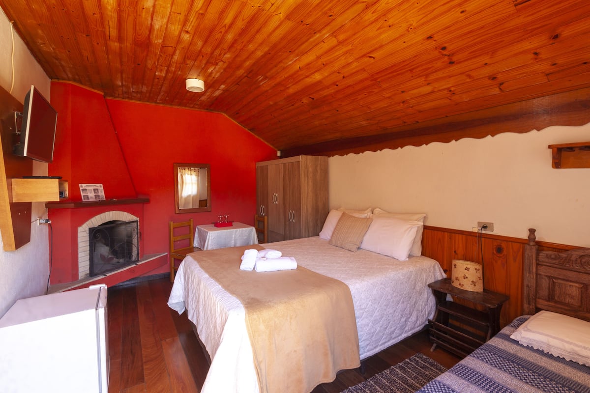 Ein Schlafzimmer mit Holzbalkendecke, Kamin, einem Bett mit weißer Bettwäsche und einem kleinen Tisch mit Lampe.
