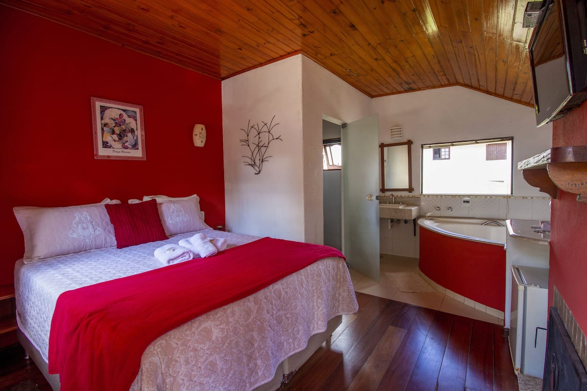 Ein Schlafzimmer mit einem Bett, einer roten Wand, einer Holzbalkendecke und einem Badezimmer mit einem roten Waschbecken.