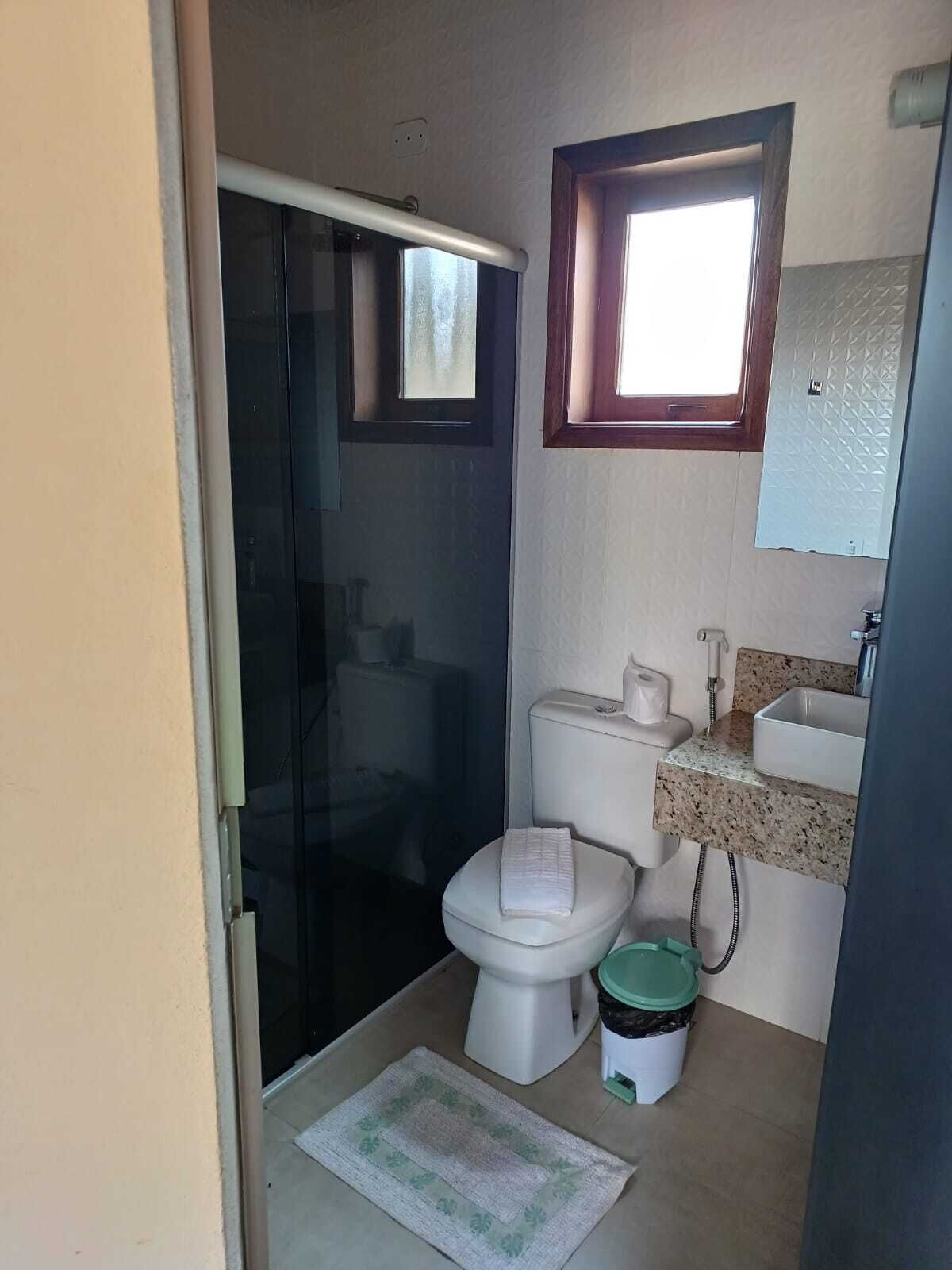 A compact bathroom with a toilet, a sink, a small window, and a shower area.