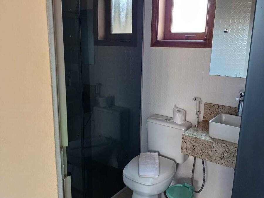 A compact bathroom with a toilet, a sink, a small window, and a shower area.