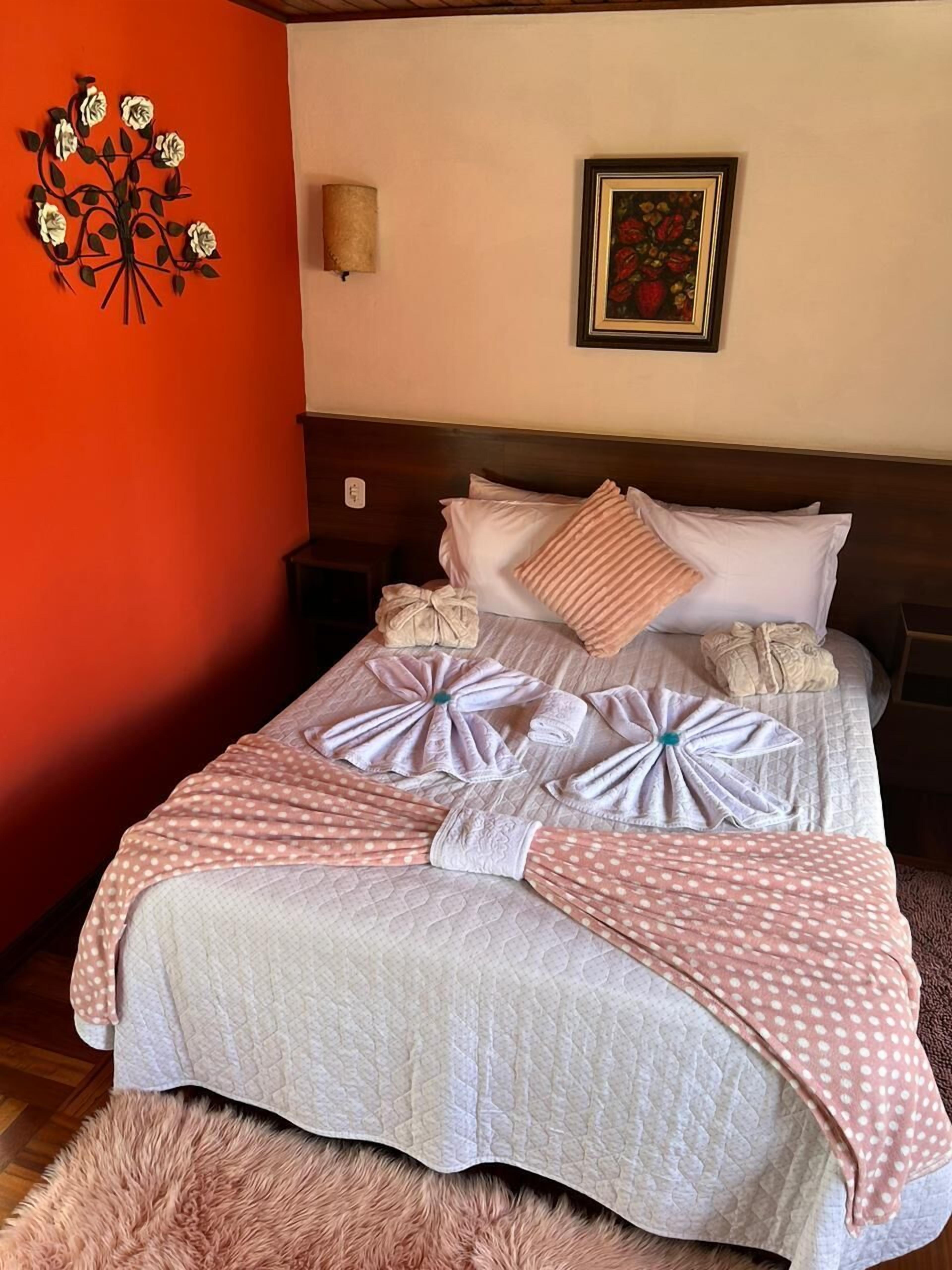 A neatly made bed with a pink polka dot blanket, a fluffy rug, and a wall decoration of flowers.
