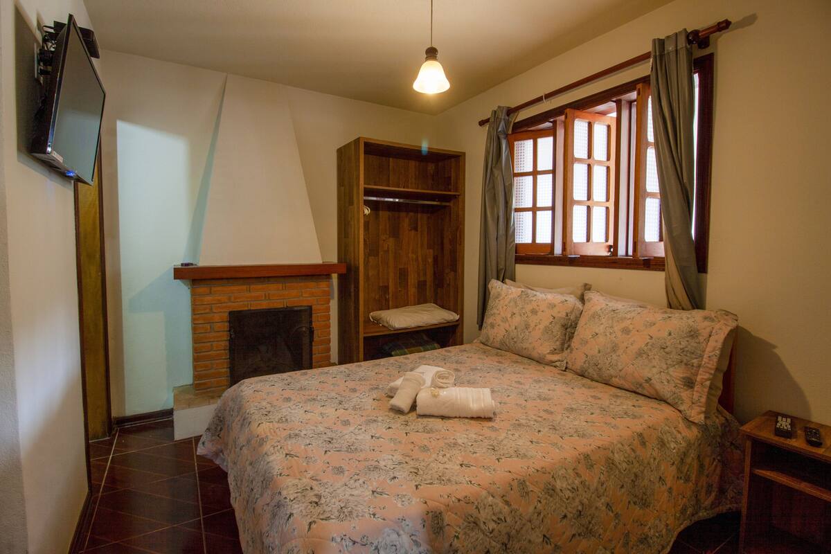 Ein Schlafzimmer mit einem Bett, einem Holzschrank, einem Kamin und einem Fenster mit Vorhängen.