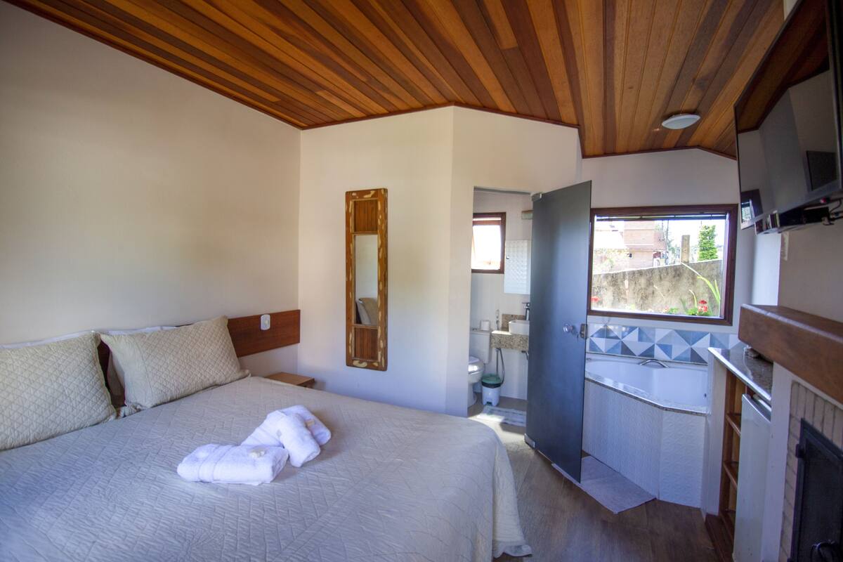 Ein Schlafzimmer mit einem großen Bett, einer Holzbalkendecke, einem Badezimmer mit einer Badewanne und einem Fenster mit Blick.