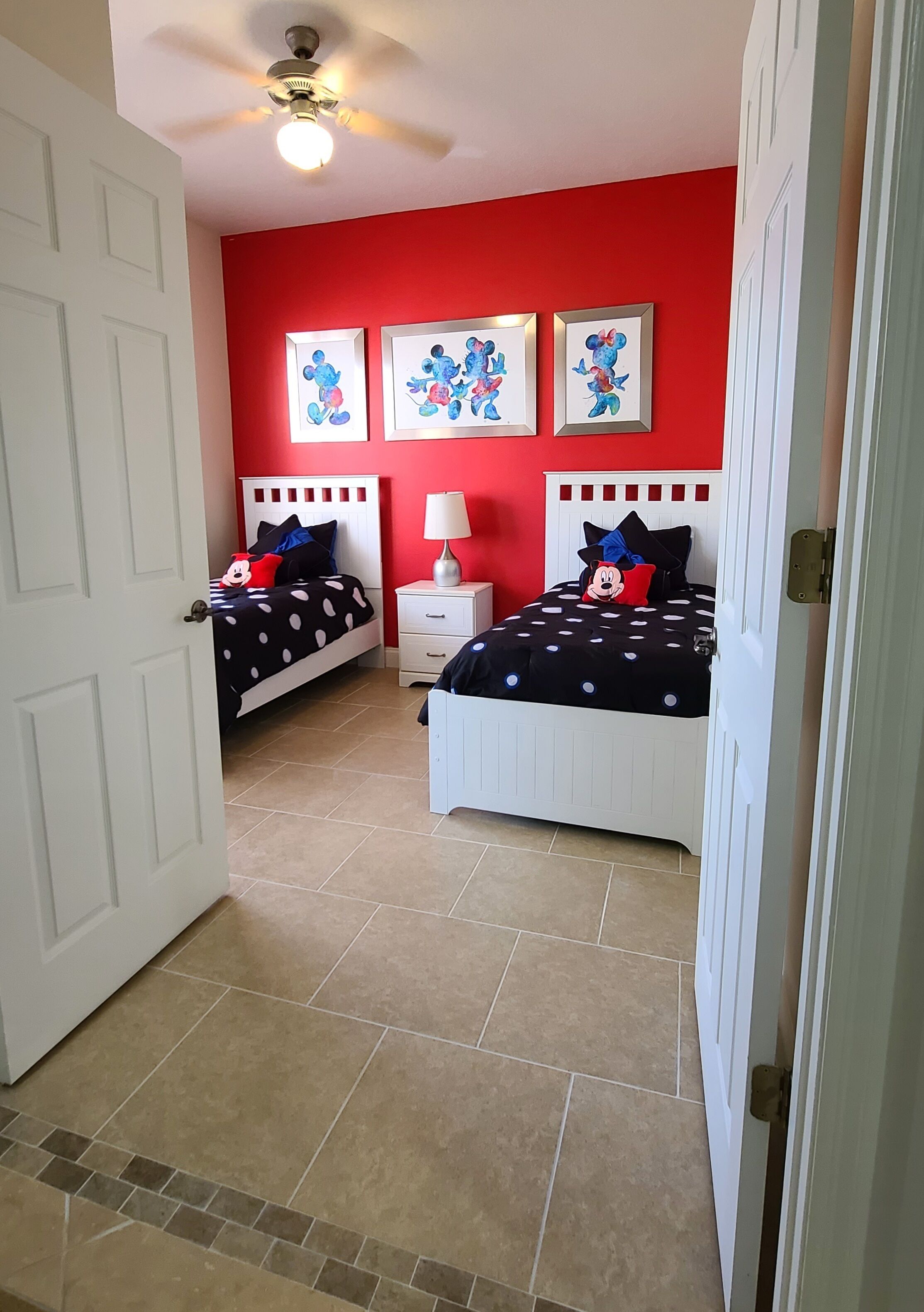 A bedroom with two beds, red walls, and Mickey Mouse themed decorations.