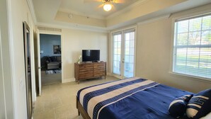 Un dormitorio con una cama, un televisor sobre una cómoda y una puerta que da a otra habitación.