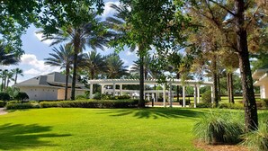 Un jardín cuidado con un quiosco blanco, palmeras y césped.