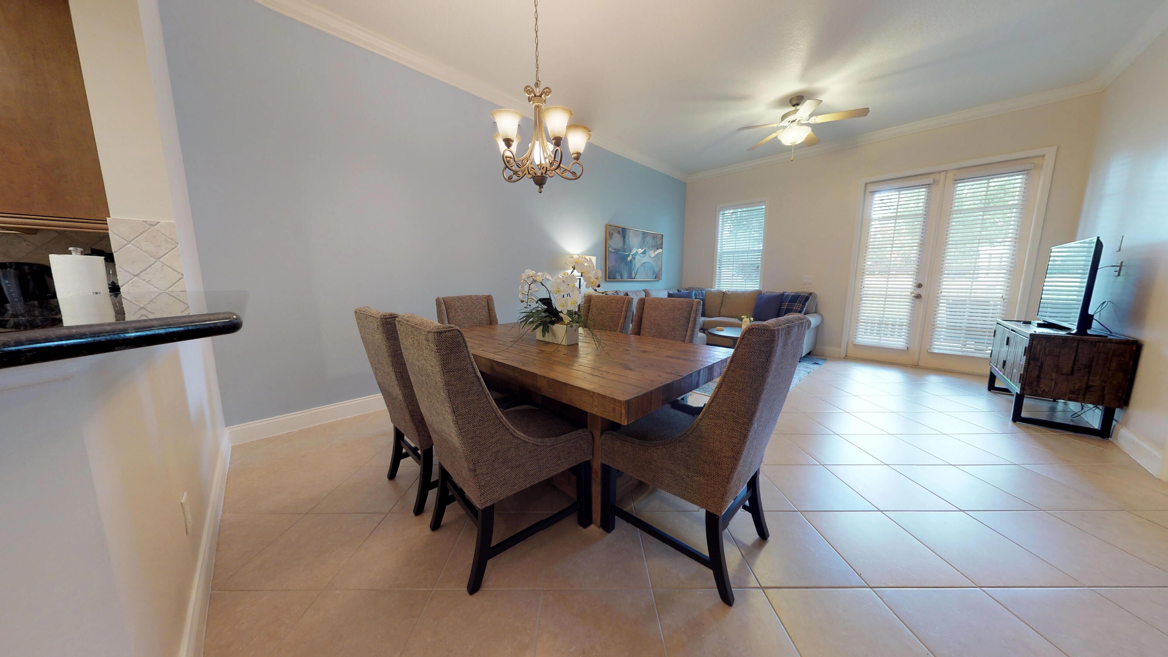 A dining area with a wooden table and chairs, a chandelier, and a ceiling fan.