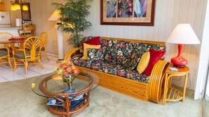 A living room with a sofa, a coffee table, a dining area with chairs, a red lamp, and a framed picture on the wall. - Hale Kamaole 220 Second floor condo, easy access to best beach on Maui! (Kihei)