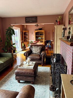 A cozy living room with a brown leather sofa, a matching ottoman, and a wooden coffee table. There is a bookshelf with decorative items and a fireplace with a mantel. - Lovely ranch home getaway in The Berkshires- just 6 miles to Tanglewood (Richmond)