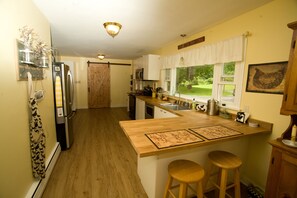 A kitchen with wooden countertops, a built-in island with stools, a refrigerator, and a window with a view of the outdoors.