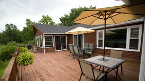 Una terraza de madera con mobiliario exterior, incluyendo una mesa y sillas, y un paraguas grande.