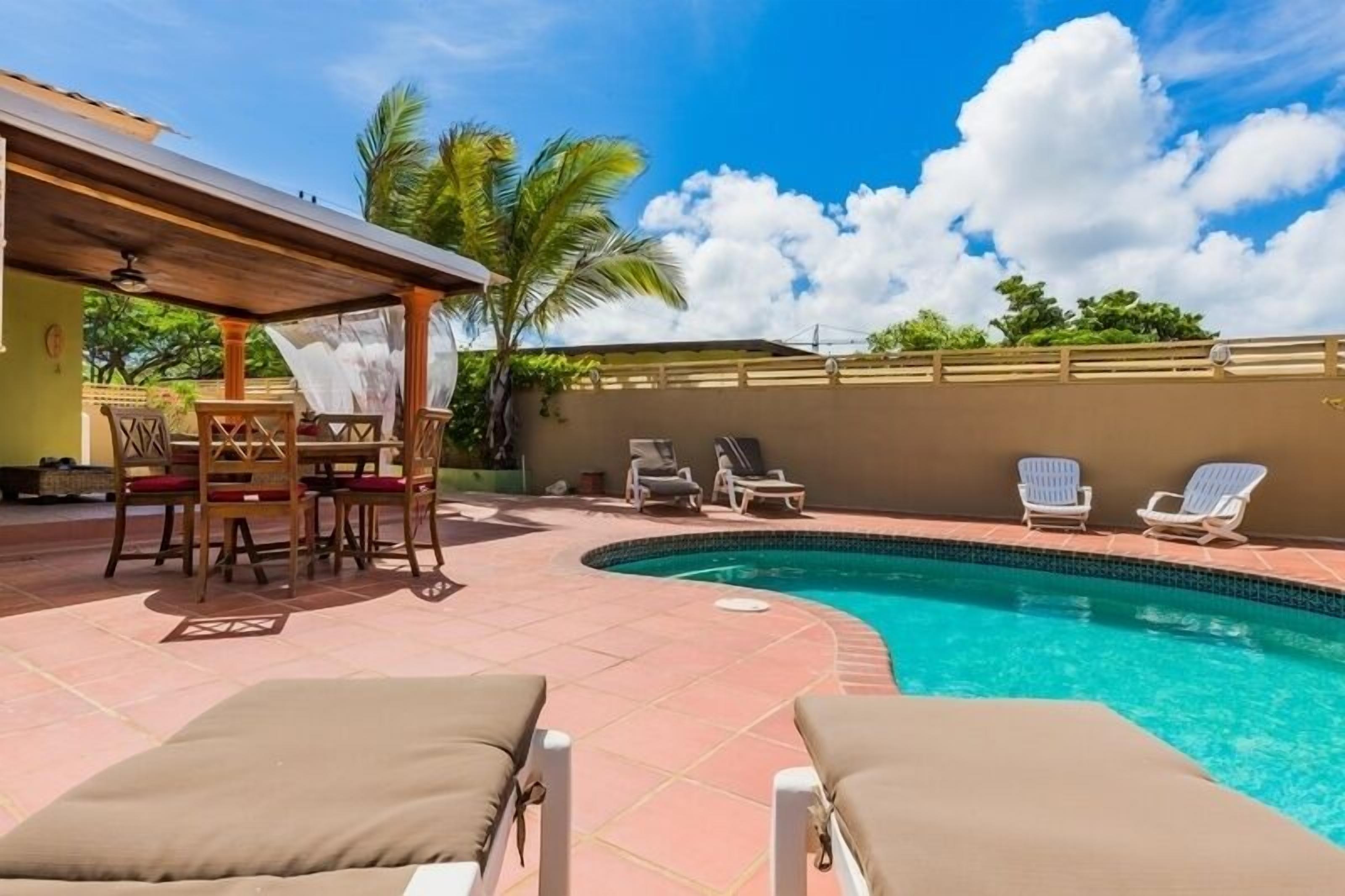 Ein Poolbereich mit Liegestühlen, einer überdachten Lounge und einem Esstisch.