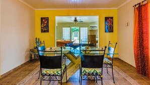 A dining area with a glass table and chairs, yellow walls, and a red curtain. - Palm Beach home with private pool (Noord)