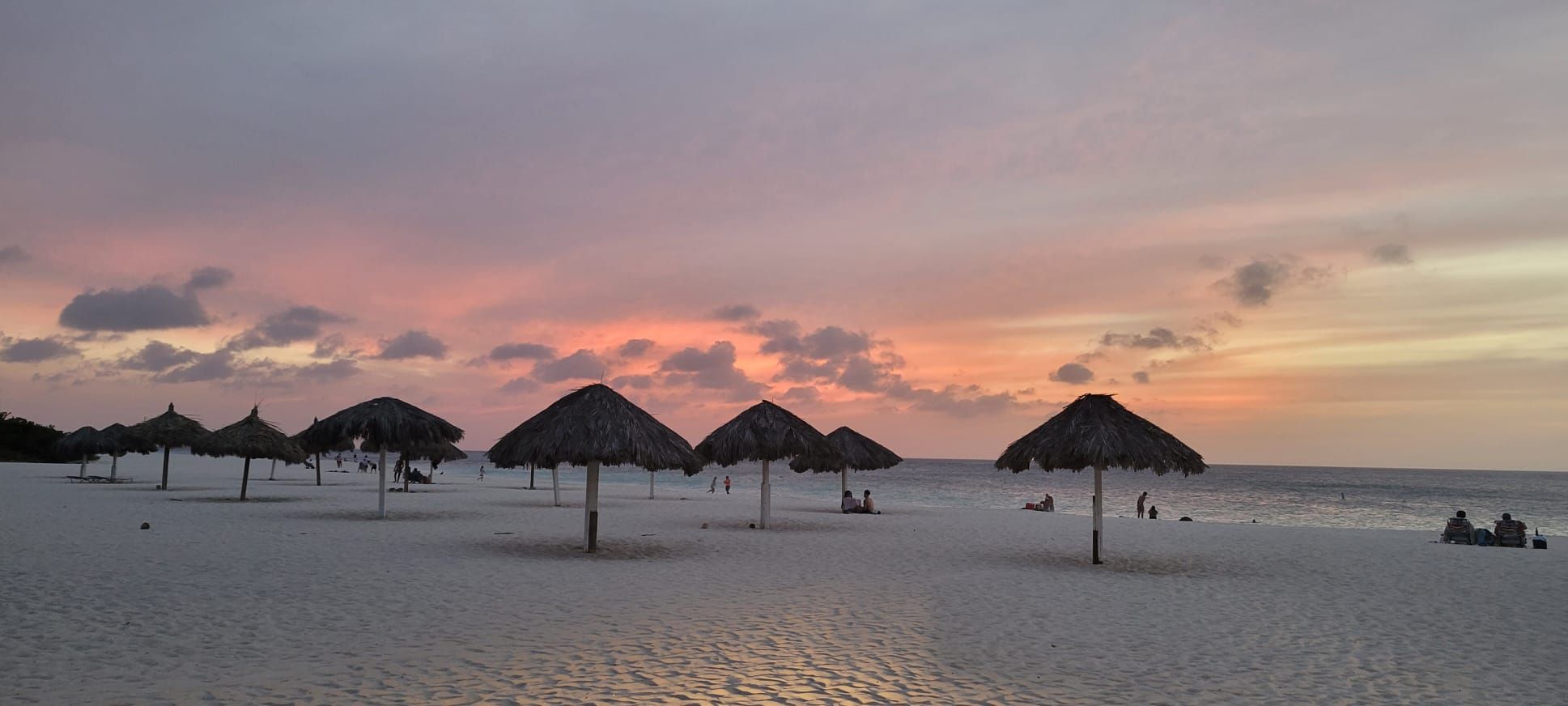 A beach with thatched umbrellas and a calm sea at sunset.