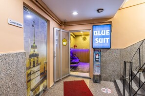 A hotel entrance with a glass door, a red carpet, a blue sign, and a security camera. - Blue Suit (Istanbul)